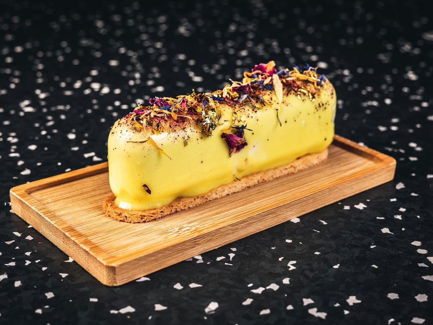 <p>Vanilla mousse filled with passion fruit and almond bisquit, passion fruit glaze with dried flowers&nbsp;</p>